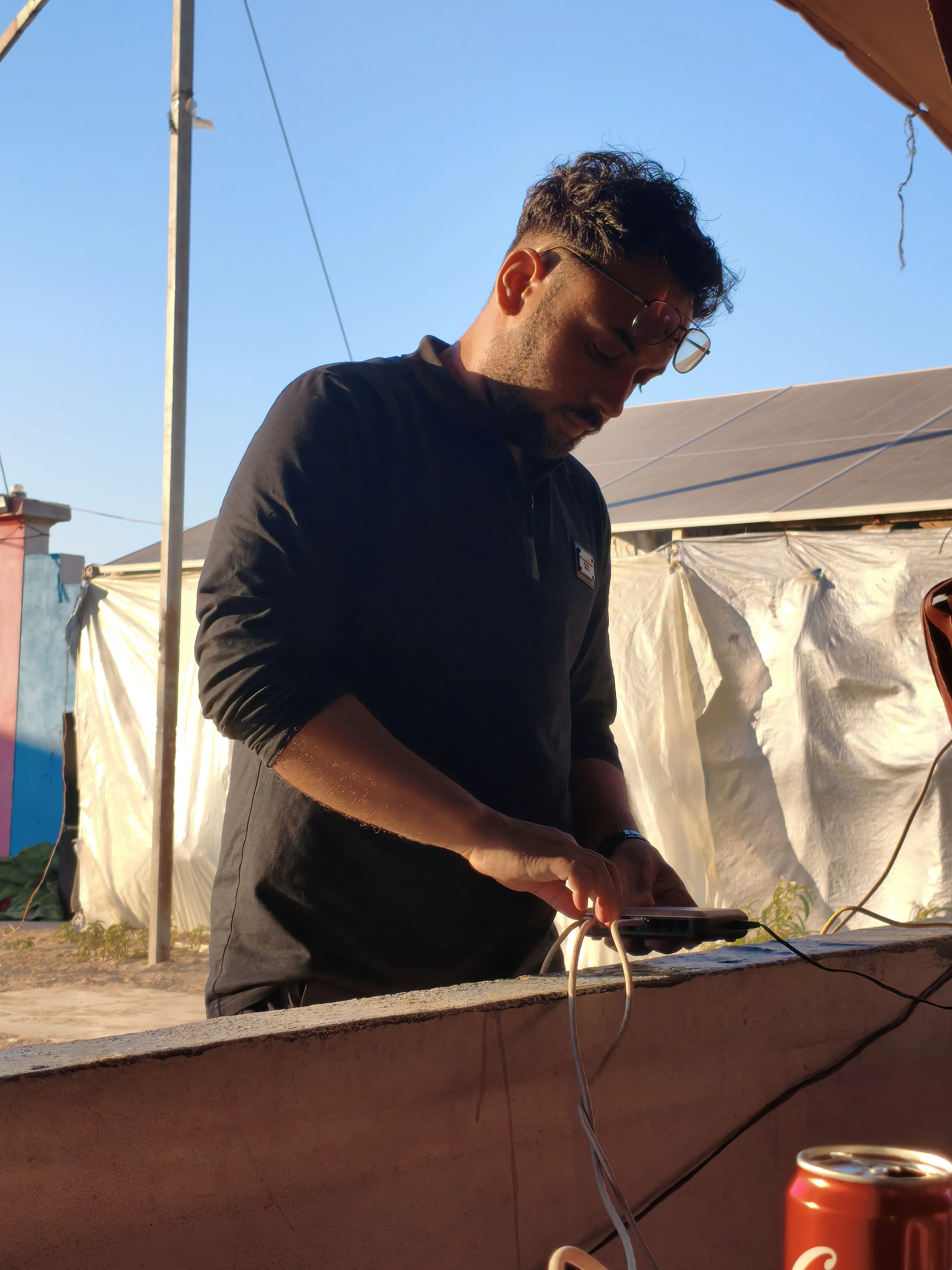A Riva Hub team member connecting equipment outdoors, with solar panels and shelter tents behind